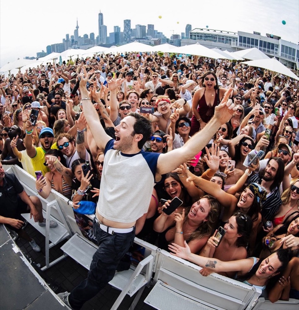 Two Friends on stage with arms up in front of a huge outdoor crowd