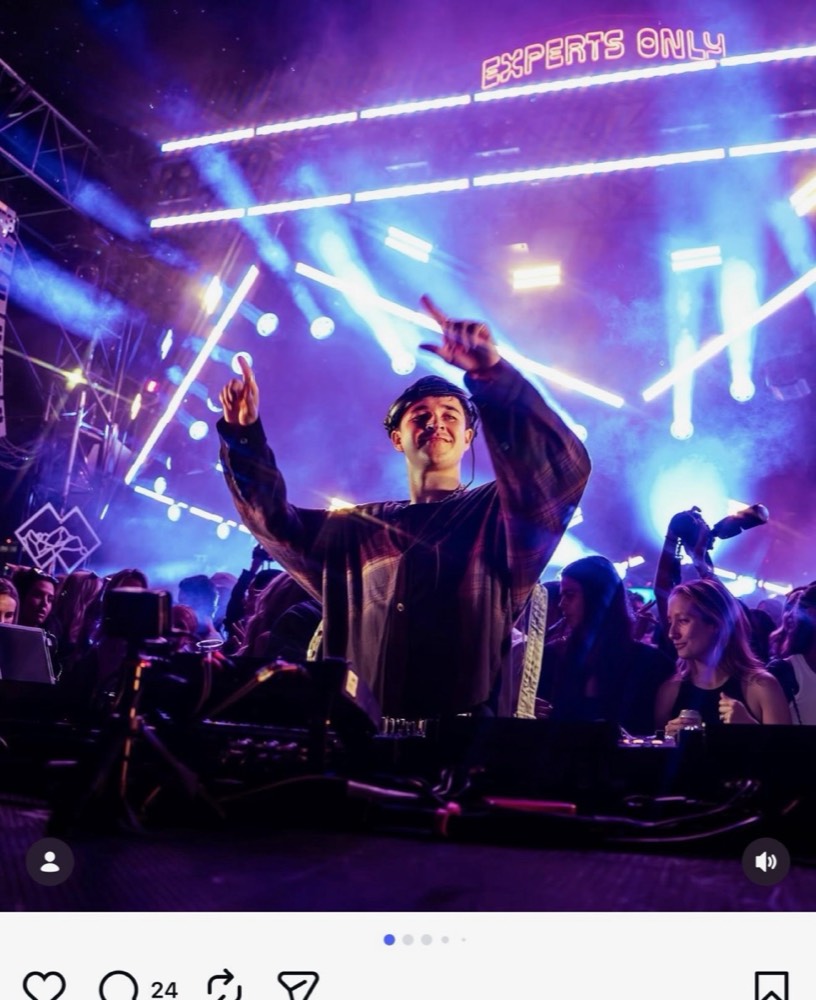 DJ with arms raised behind the decks under purple lights