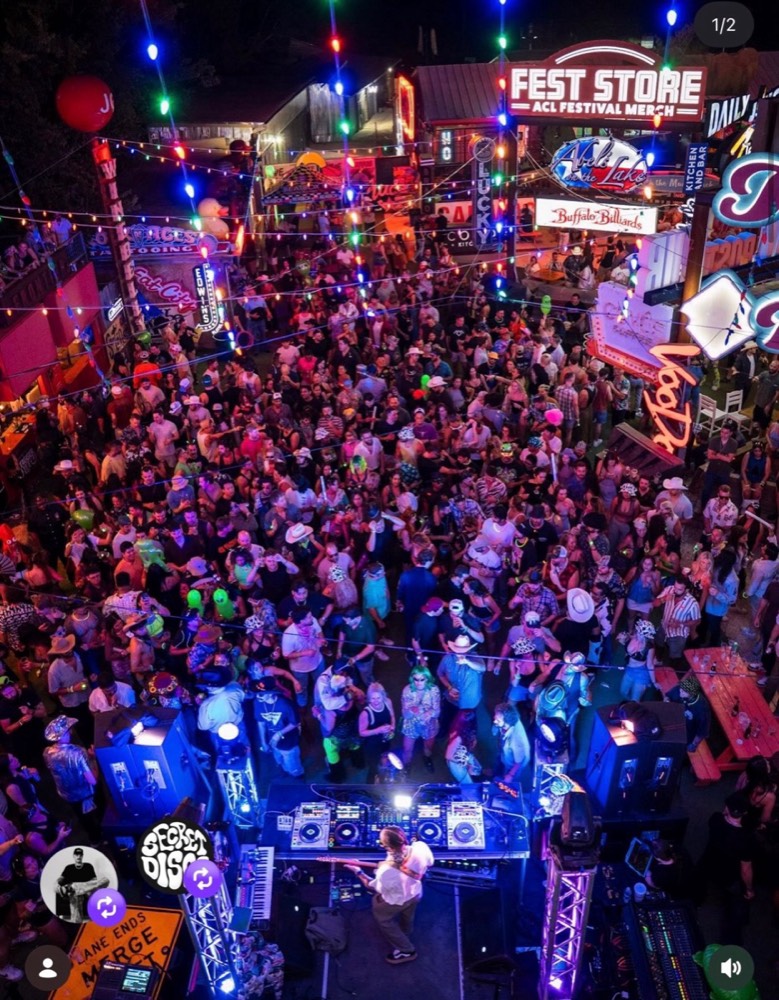 Outdoor festival crowd around a DJ booth under string lights