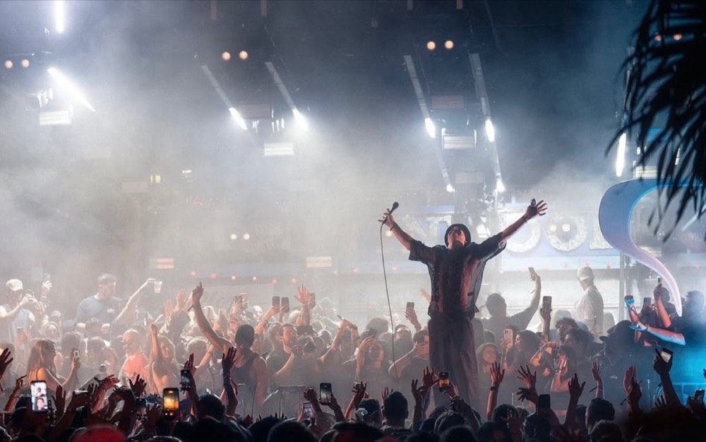 Performer with arms outstretched in front of a crowd in an open-air venue