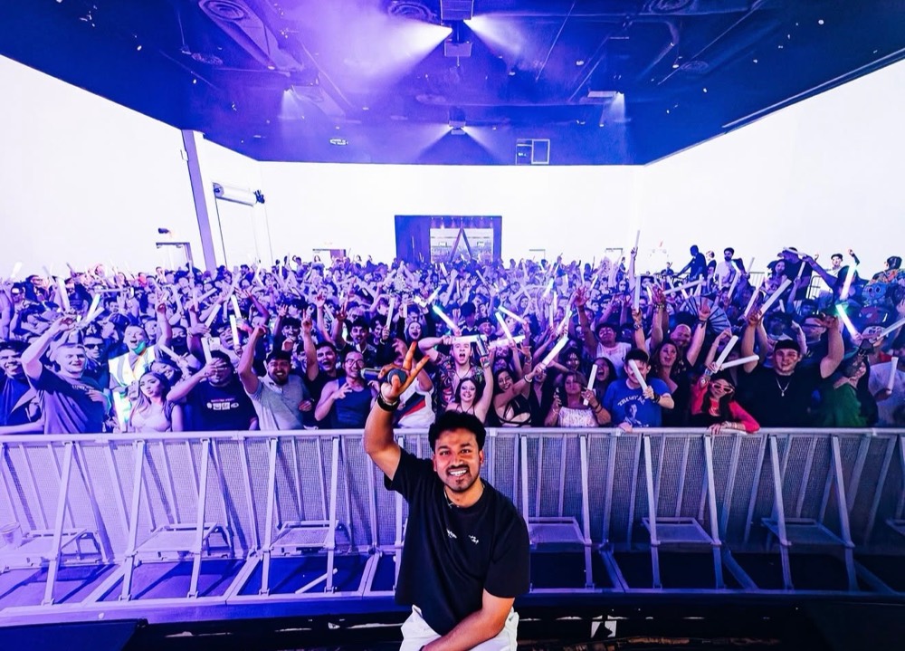 DJ with an arm raised in front of a crowd holding glow sticks