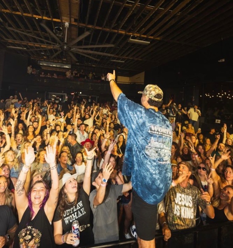 Artist at the edge of the stage pointing into a full room