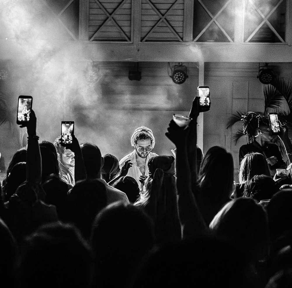 Black and white shot of a DJ behind the decks as the crowd holds up phones