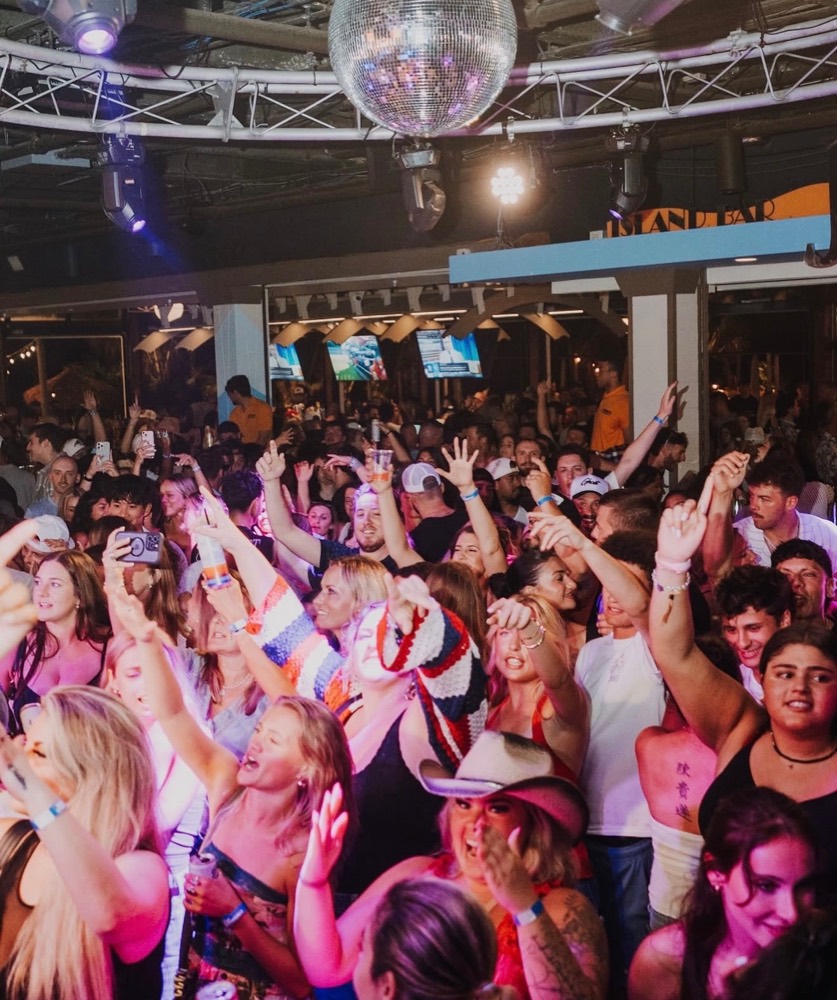 Packed crowd with hands up under a disco ball at the Island Bar